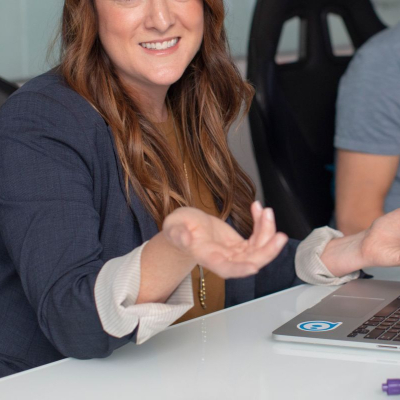 woman with long hair and a blazer shrugs during a conference meeting