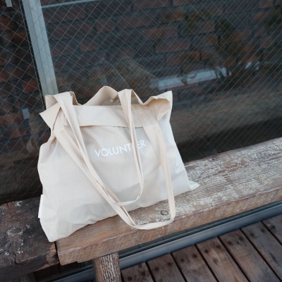 white tote bag sits on a bench; tote bag reads "VOLUNTEER" in white lettering