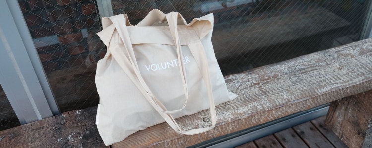 white tote bag sits on a bench; tote bag reads 