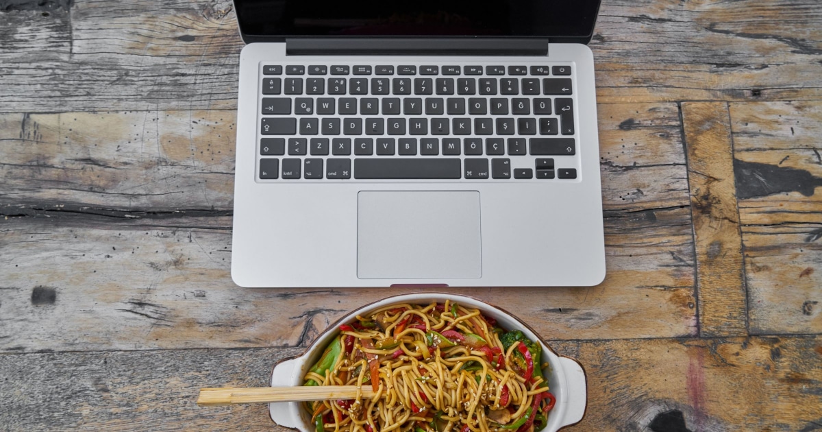 image of lo mein noodles and wooden chopsticks in front of a laptop computer
