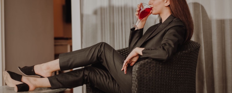 overachieving woman is drinking alcohol; she wears a brown suit and has her feet up