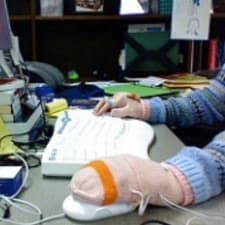 professional woman working at computer, wearing USB-heated mittens as she types and uses her mouse