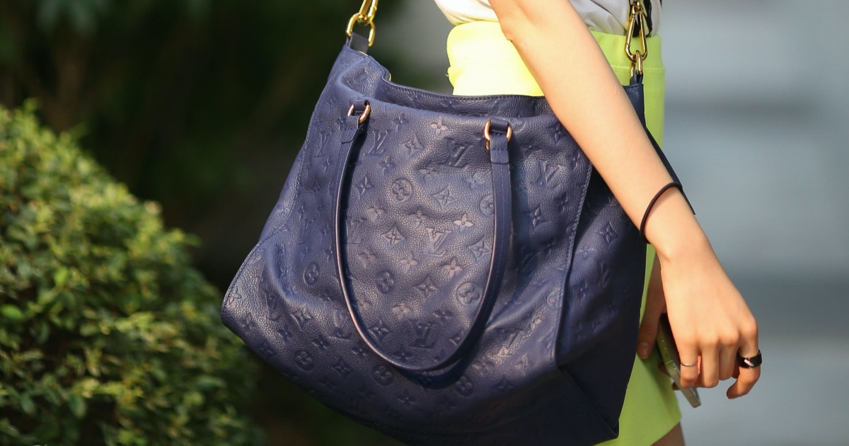 professional woman has a messenger-style navy bag with LV logos over it