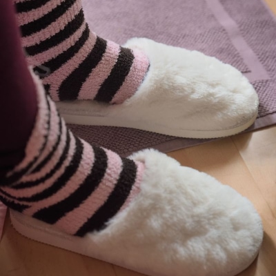 person wears pink stripey socks with fuzzy slippers