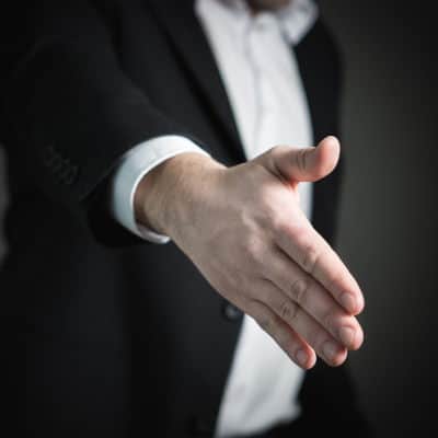 person wearing suit holds out hand for a handshake