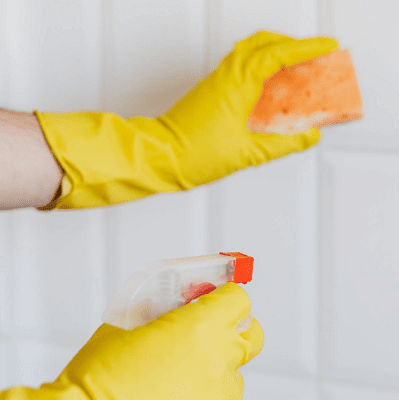 hands wearing yellow gloves spray a door, the left hand holds an orange sudsy sponge