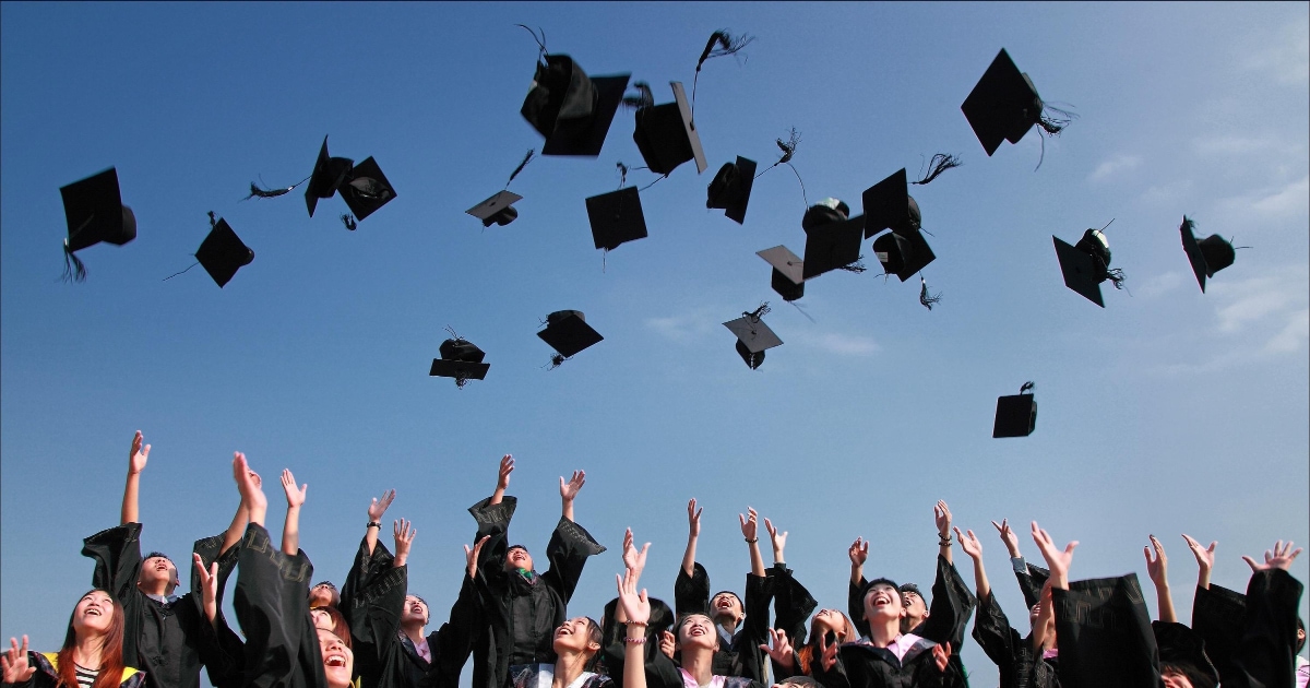 group of people throw black graduation caps into the air