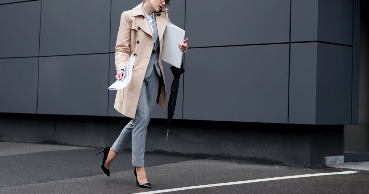 a stylish professional woman walks to work, trying to carry too many things in her hands -- she could use a great bag for walking to work
