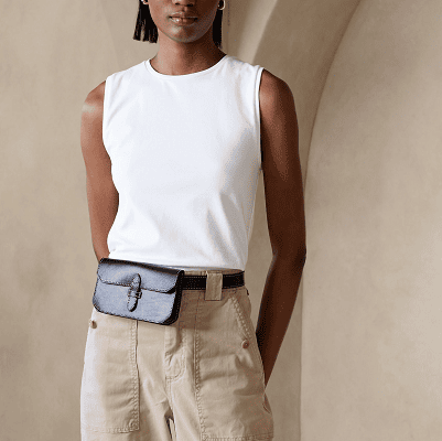 woman wears dressy tank for the office; she wears a white sleeveless tee with beige pants and a brownish blackish belt bag