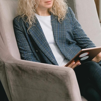 woman wears a dressy t-shirt with a blazer; she is reclining in an armchair and reading an ipad