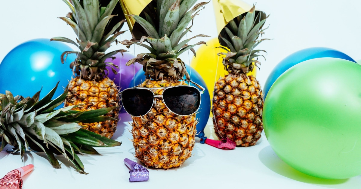 pineapples wearing sunglasses and party hats surrounded by balloons
