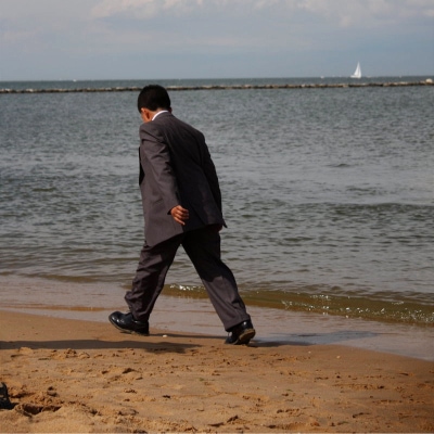 man wearing a suit and dress shoes walks along a beach