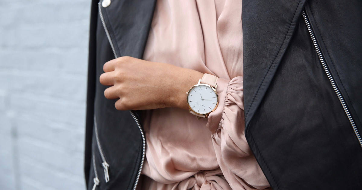 woman wears wristwatch and pulls her leather moto jacket closed over her peachy silk dress