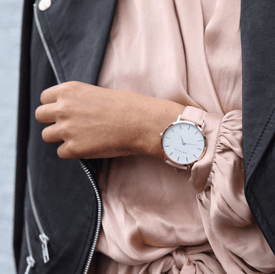 woman wears wristwatch and pulls her leather moto jacket closed over her peachy silk dress
