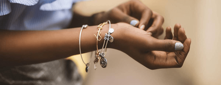 woman holds out a wrist with three bracelets on it; she has brown skin and is wearing light blue nailpolish. 