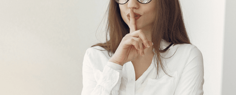 young professional woman holding her finger up to her lips to say 