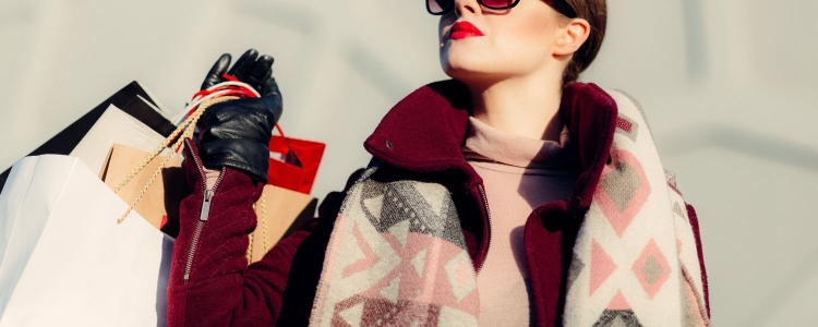 fashionable woman wears sunglasses and overcoat, and carries several shopping bags over her shoulder