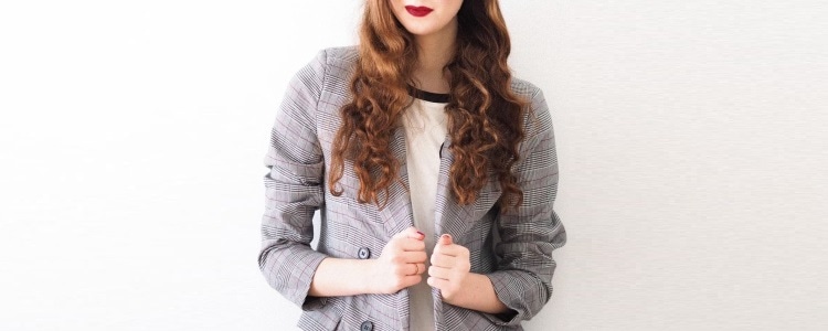 woman with red hair wears an oversized double-breasted blazer over a ringer tee; she is pulling the blazer closed and is wearing dark red lipstick