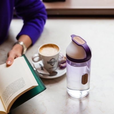 professional young woman reads a book with a latte and water bottle next to her