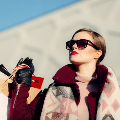 fashionable woman wears sunglasses and overcoat, and carries several shopping bags over her shoulder