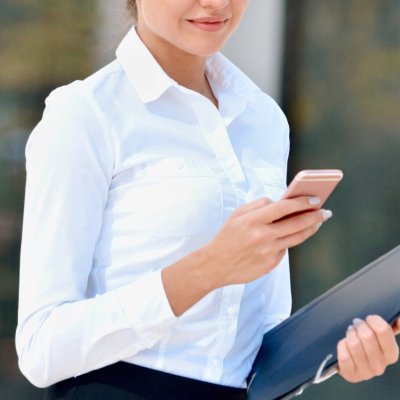 stylish businesswoman wears a button-front shirt, looks at her phone and carries a folder