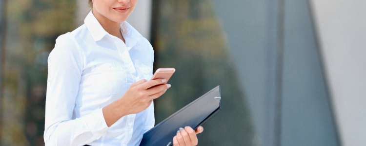 stylish businesswoman wears a button-front shirt, looks at her phone and carries a folder