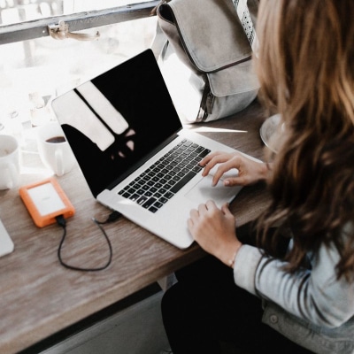 woman works on laptop; there is an orange cell phone charger in view as well