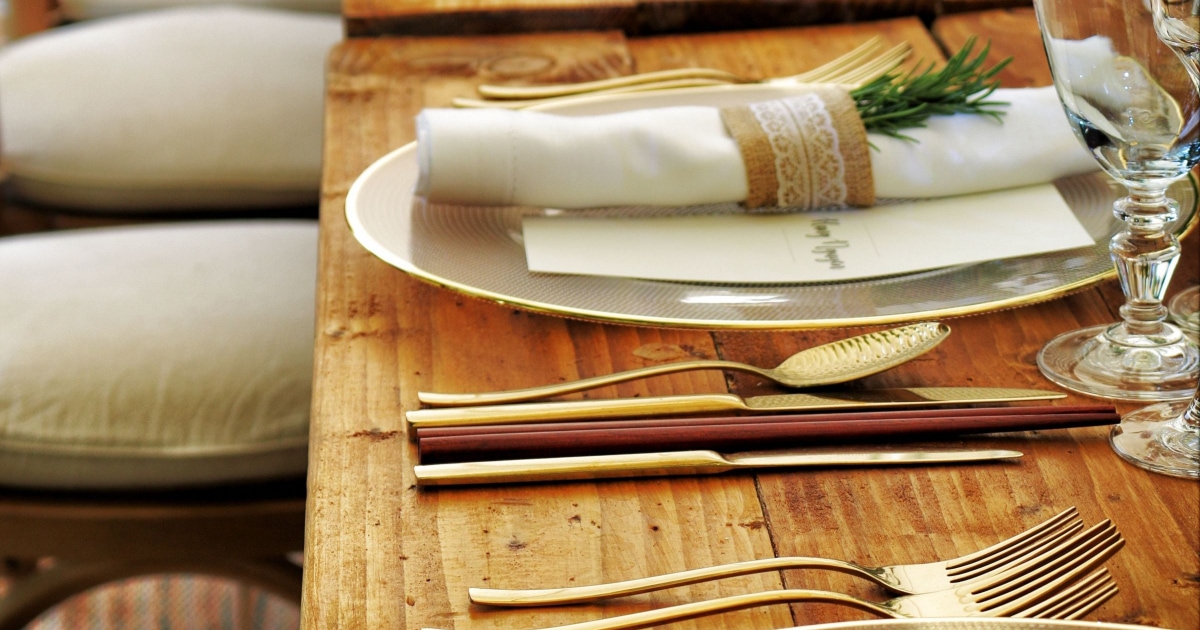 table set beautifully with gold silverware, chopsticks, and rolled napkins with sprigs of holly