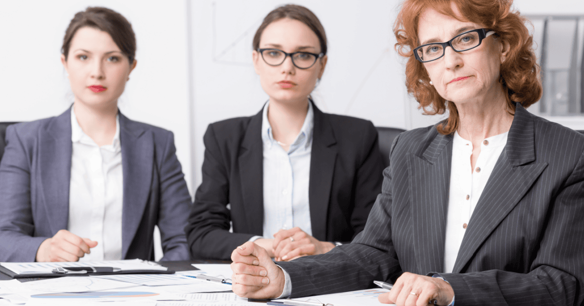three stern looking women wear suits; you're in tro-uh-ble