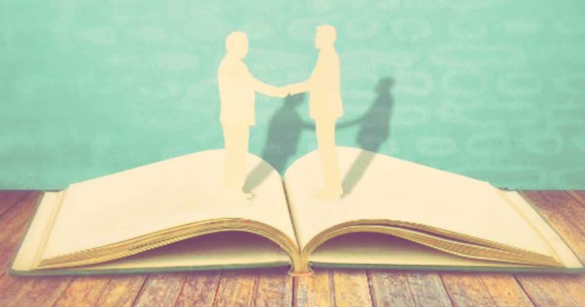 artistic rendering of two people shaking hands and possibly one is a woman building her book of business -- the figures look like cardboard cutouts sitting on top of an open book. 