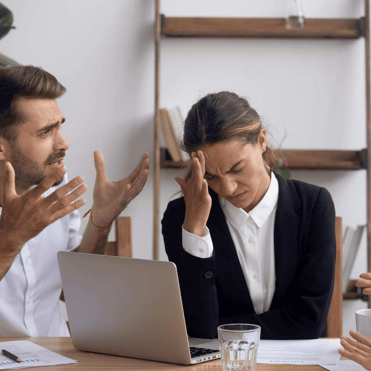Woman hangs her head while a male colleague talks beside her during a meeting