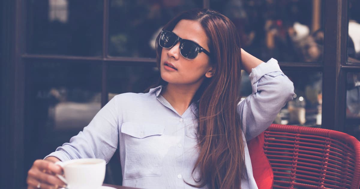 young professional woman looks hot while sitting outside; she is wearing summer work clothes of a blue button-front shirt and black pants