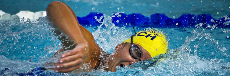 woman swims in pool; she wears a yellow swim cap and goggles