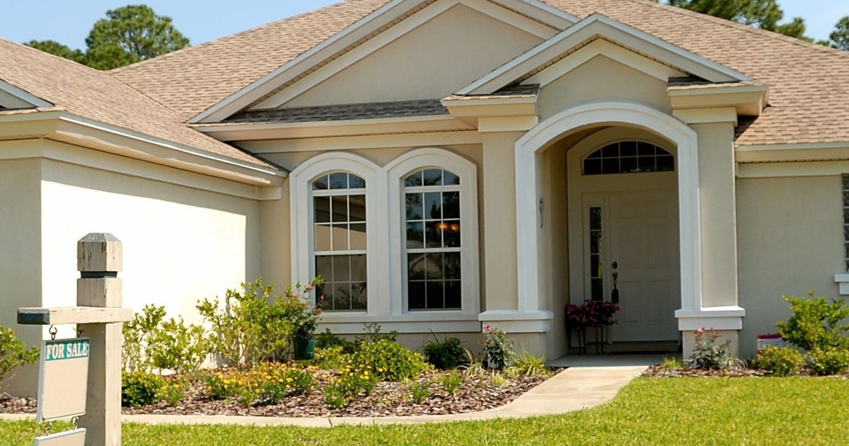 beige house with "for sale" sign in front