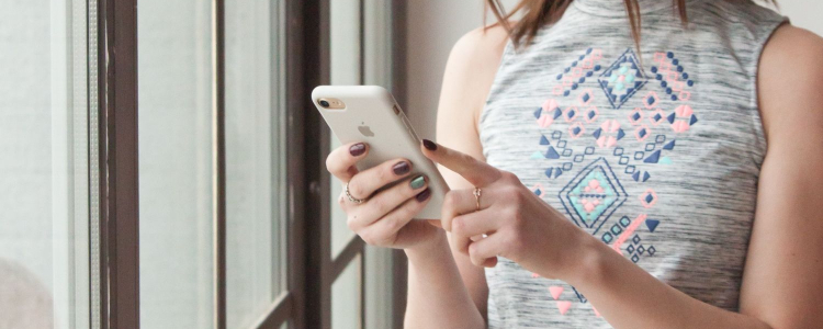 woman wearing sleeveless work dress texts on her phone while standing by window