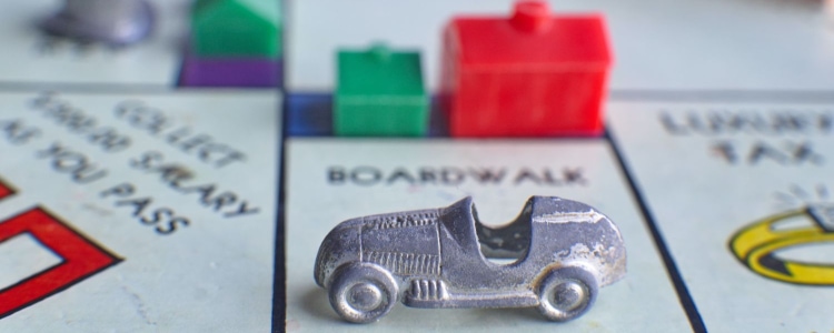 Monopoly gameboard with silver car on Boardwalk; there is a red hotel and a green house