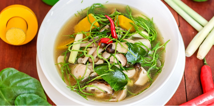 bowl of soup with lots of greens, mushrooms, and a chili pepper