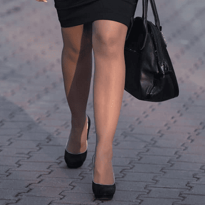 woman wears pantyhose and a black pencil skirt while walking down street with interlocking bricks