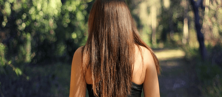 woman stands outside, she has long brown hair and is wearing a black sports bra