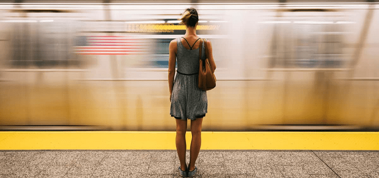 woman stands on subway platform while train passes her by; you can see a blurred American flag on the train