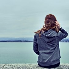 woman in a gray hoodie stares out at a sea