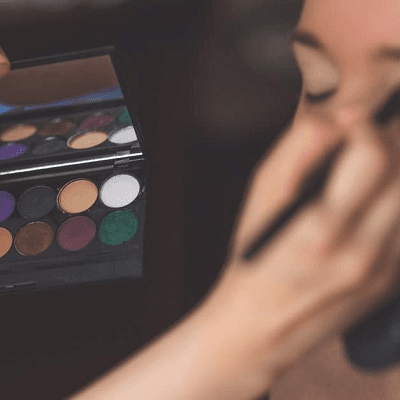 makeup artist applies eyemakeup to woman; she holds a palette of eyeshadow colors