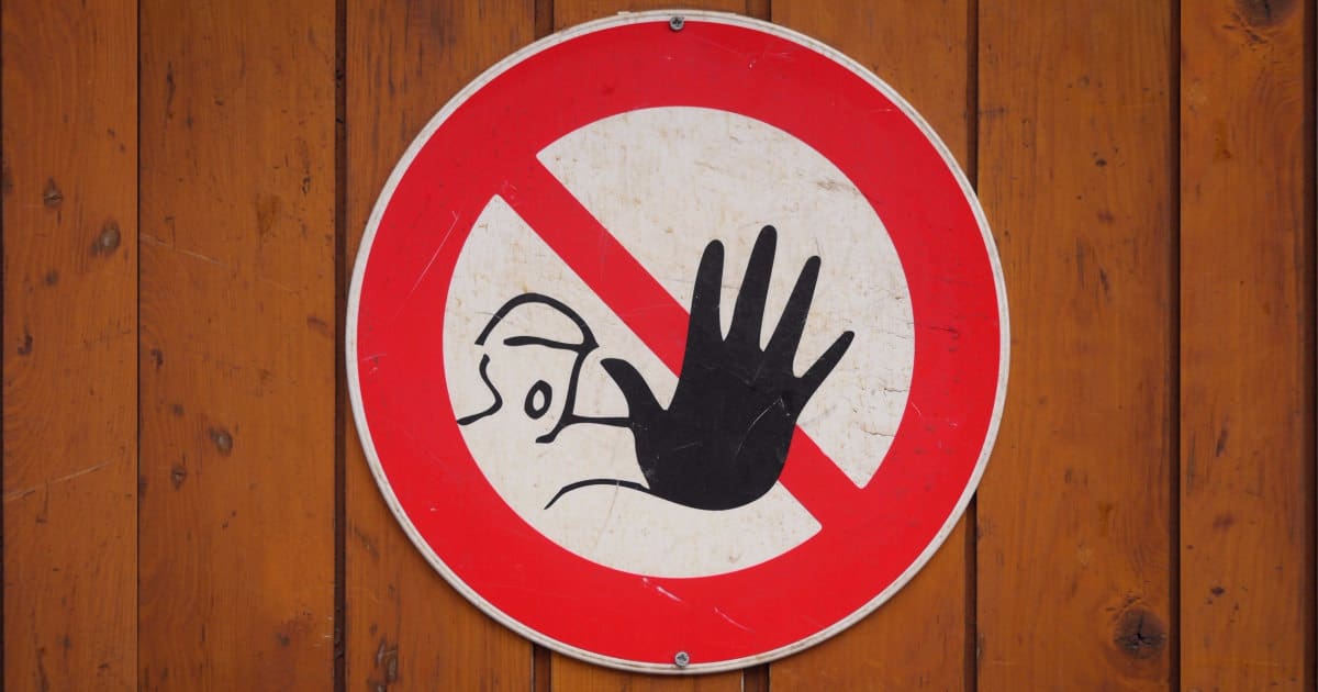 a round sign featuring a person holding up a hand with a big red "no" symbol (circle with slash)
