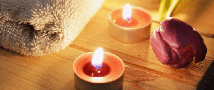 lit tea light candles, a folded beige towel, and a purple rose