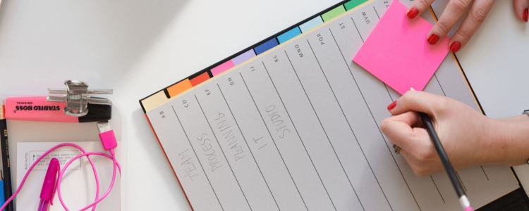 woman writing on pink post-it in a planner with multi-colored tabs
