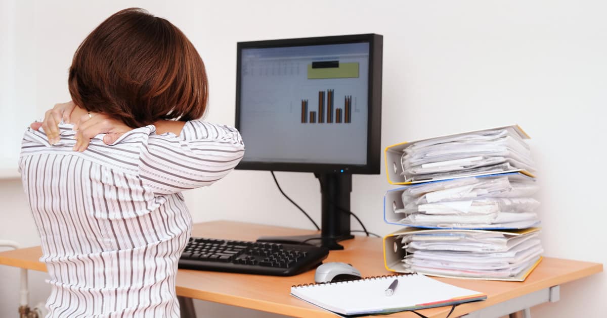 woman looking at a computer and rubbing her shoulders