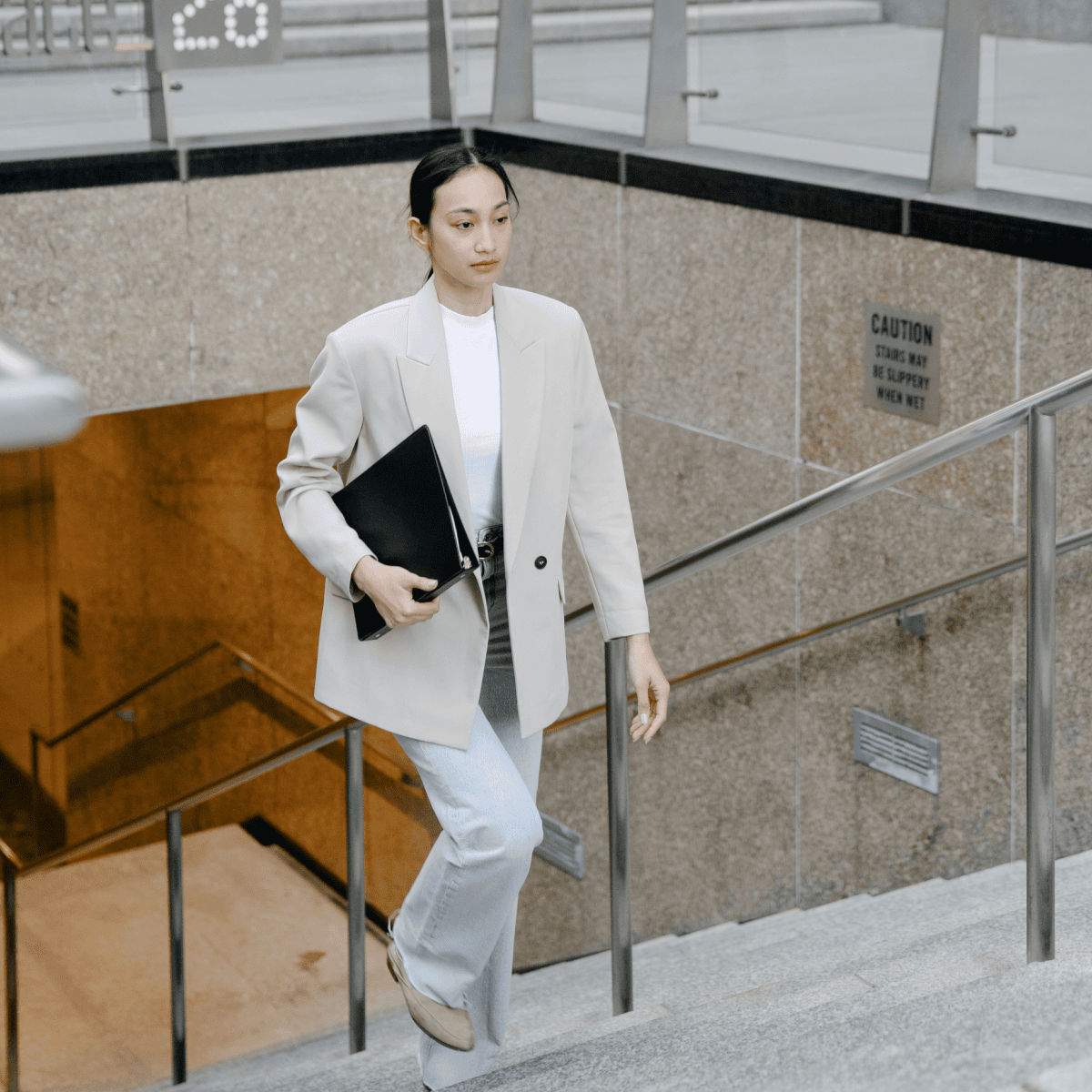 stylish woman climbs (subway?) stairs; she is wearing light jeans and a beige blazer with beige boots