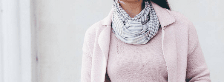 woman wears pink sweater set, there is a rip in the sweater shell that is partly covered by a scarf around her neck