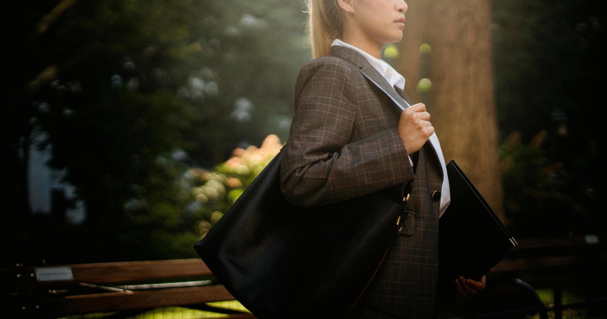 young professional woman carries a bag to her interview; she is wearing a suit, a white blouse, and has her hair in a ponytail