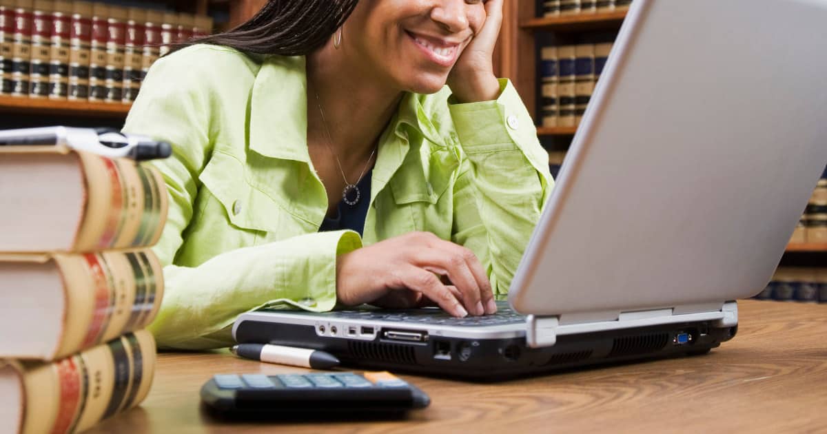 woman law student wearing a lime green shirt looks at a laptop while sitting in front of law library shelves